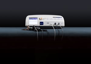 Dispositivo medico Human Tecar HCR 1002 con quattro cavi collegati e manipoli metallici appoggiati su una superficie scura. Sul display è visibile il logo 